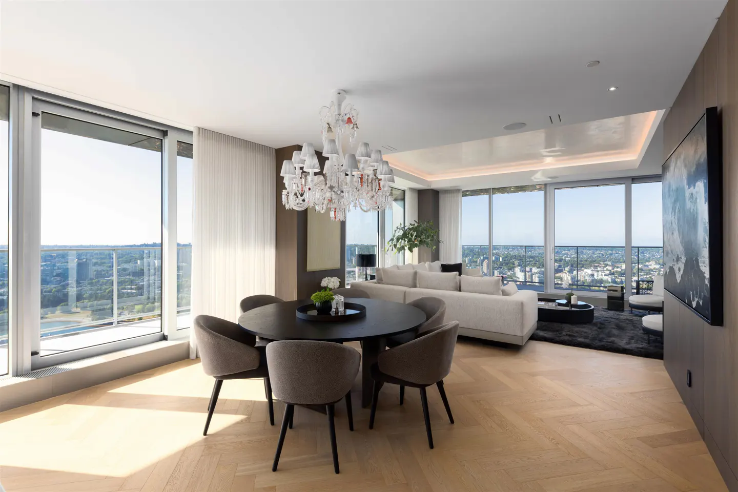 Bright, modern condo interior with a round dining table, chandelier, and floor-to-ceiling windows overlooking a city skyline.