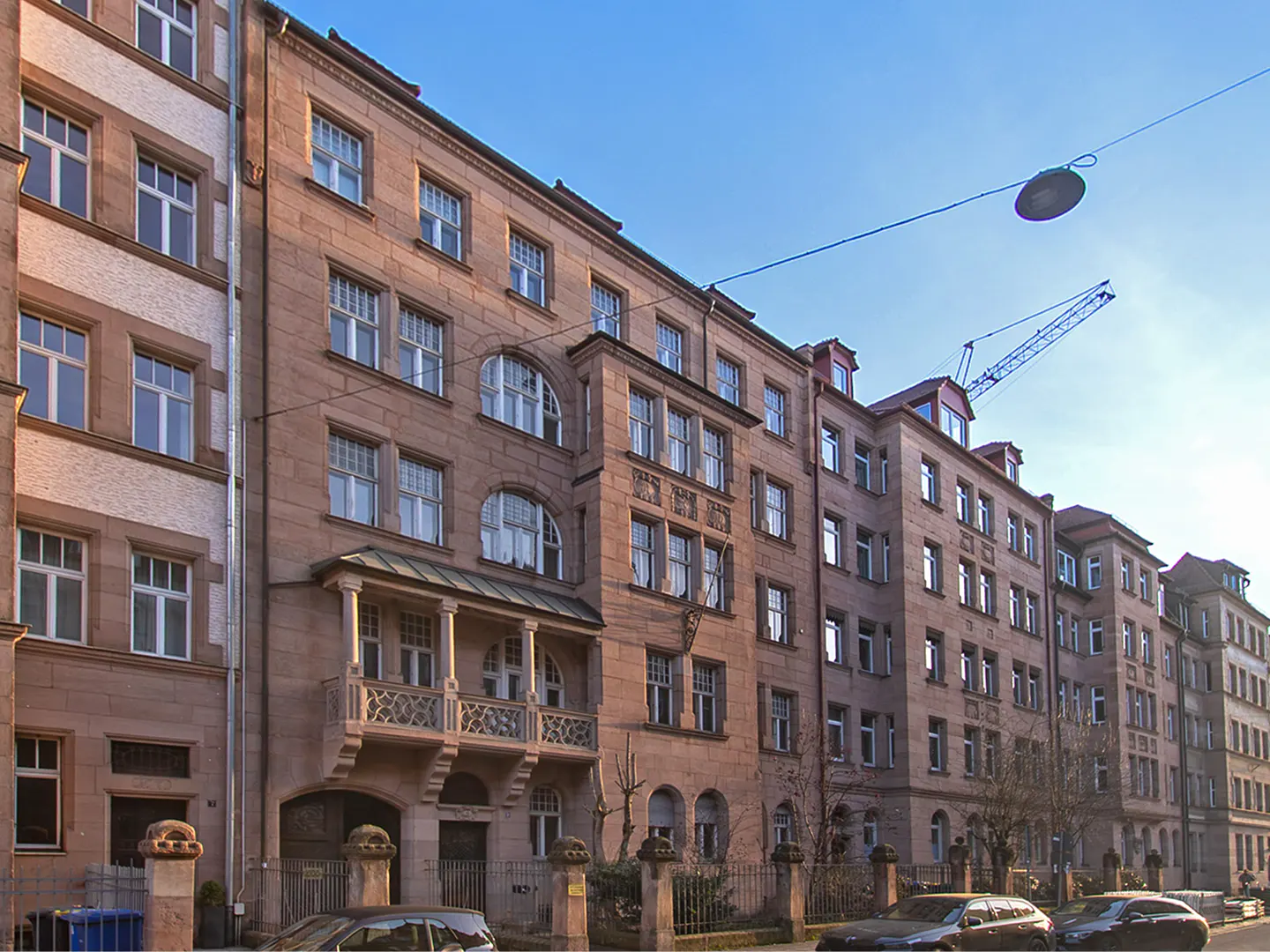 A row of multi-story brownstone apartment buildings lines a street with parked cars. A construction crane is visible in the background.