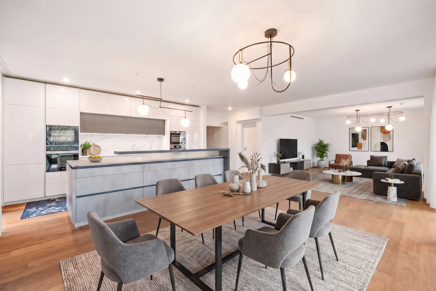 Open-concept living space with a kitchen, dining table, and living room. White cabinets and gray island. Wood table with gray chairs.