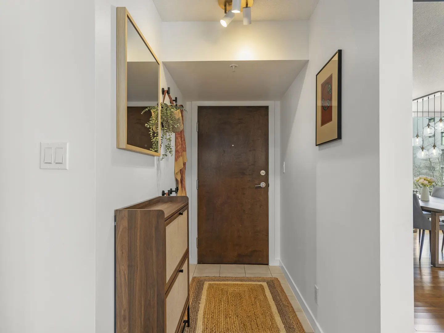 Entryway with a brown door, a jute rug, and a wooden shoe cabinet. A mirror and art hang on the white walls.