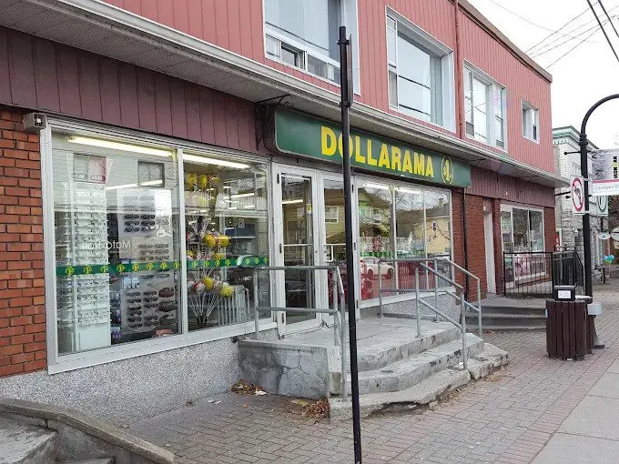 Exterior view of a Dollarama store with a green sign, glass windows displaying merchandise, and a red brick and siding facade.