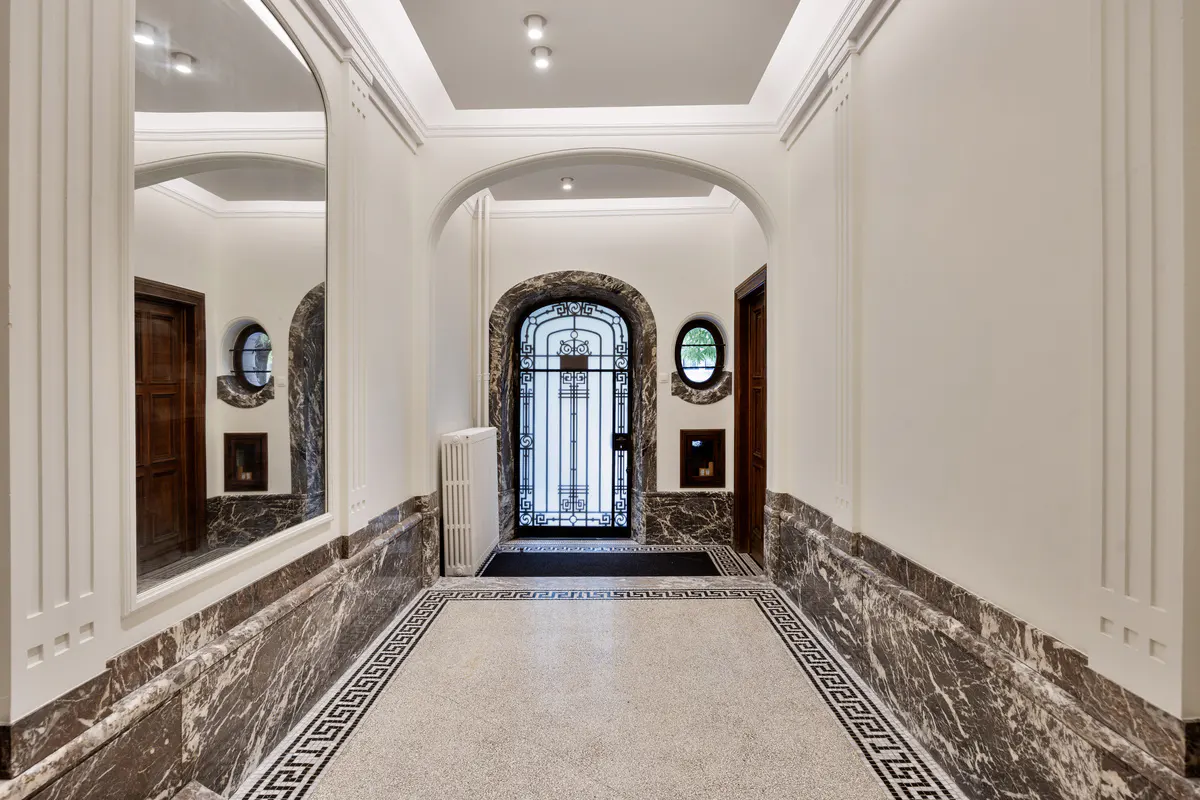 Elegant hallway with marble wainscoting, mosaic floor, and arched doorways. A decorative iron gate is visible at the end.