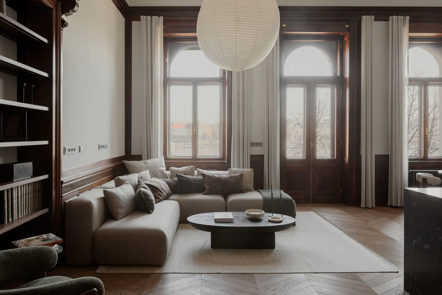 Living room with a beige sectional sofa, dark wood trim, and herringbone floors. A large paper lantern hangs from the ceiling.
