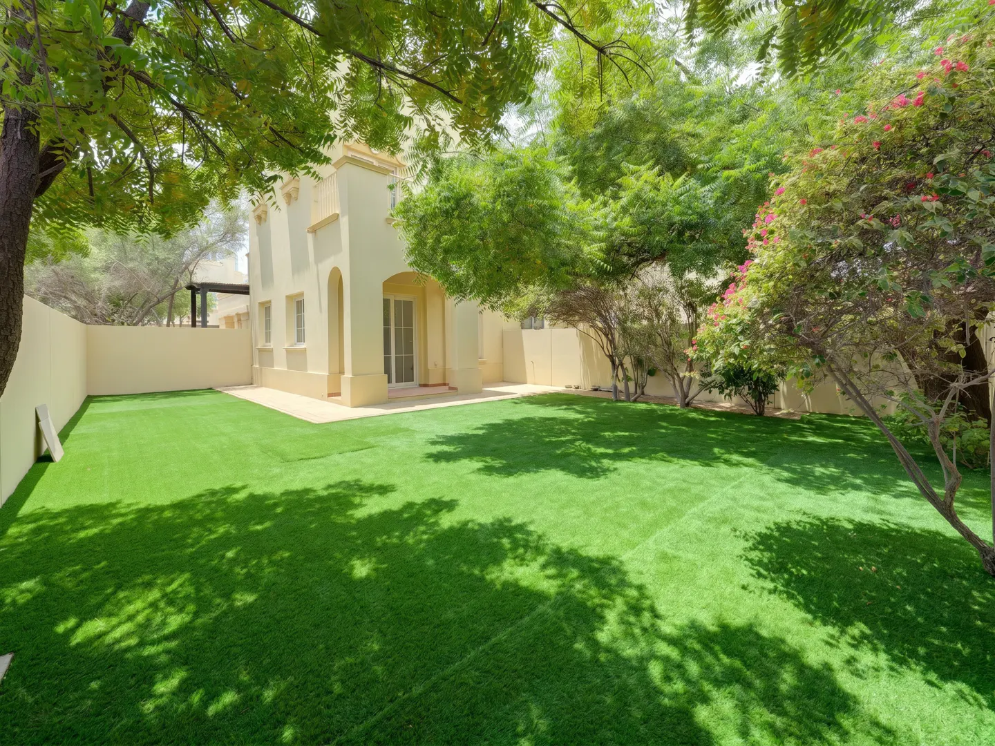 A tan house with a green lawn and trees. The house has a sliding glass door and a small patio.
