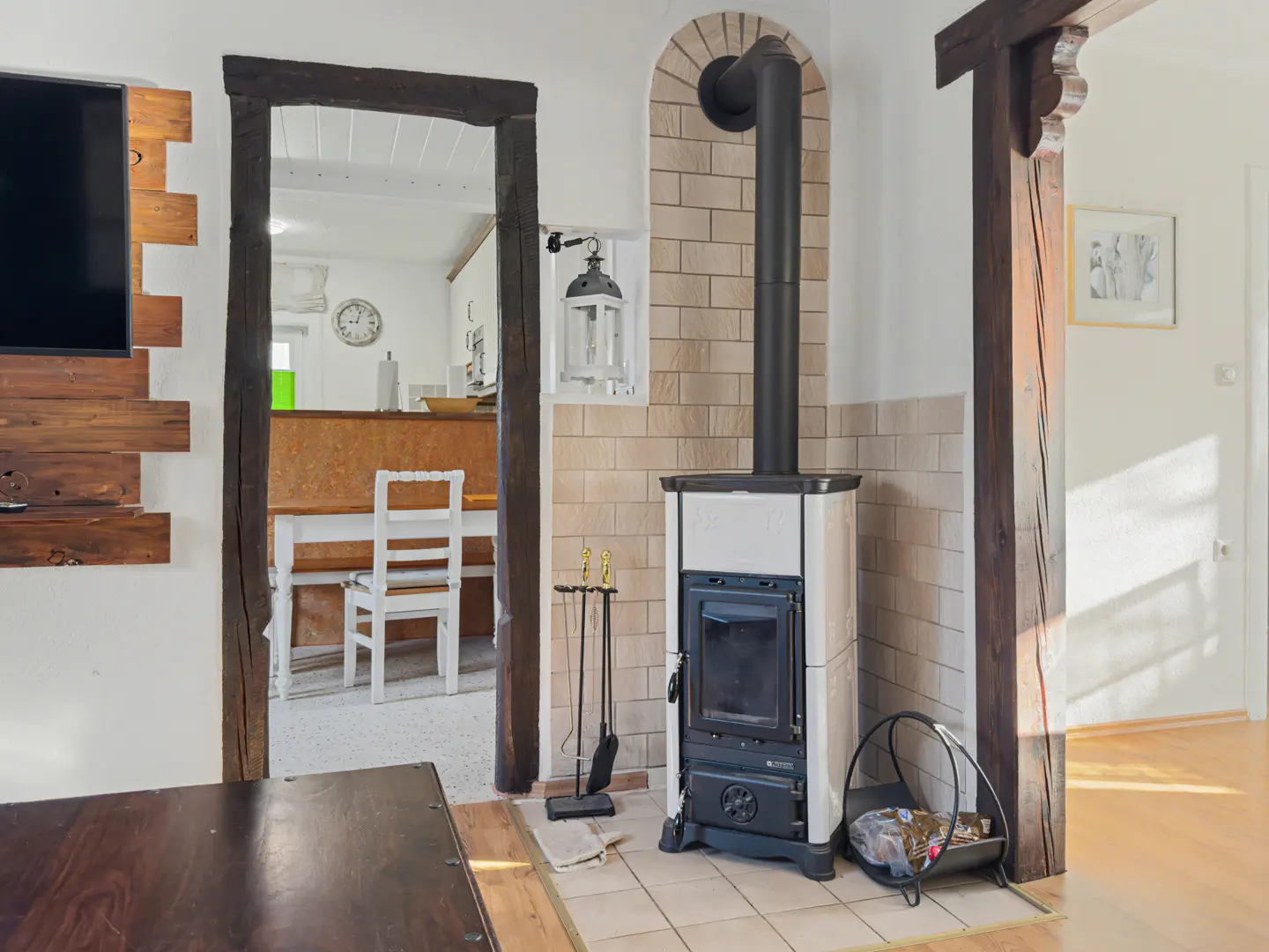 Living room with a black wood-burning stove, brick surround, and black chimney pipe. A dark wood frame doorway leads to a dining area.