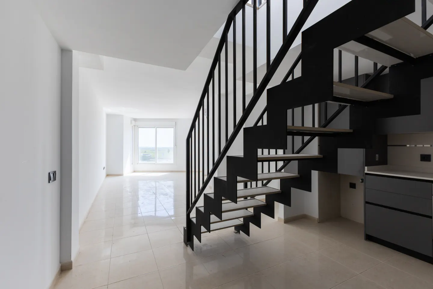 Modern interior with black metal staircase, light wood treads, and white walls. A window is visible in the background.