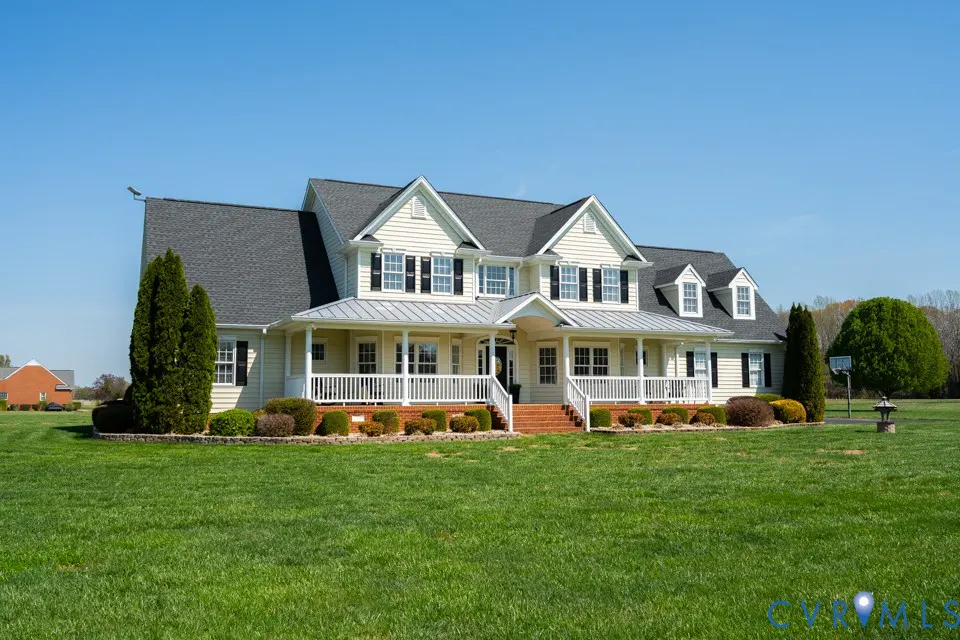 Two-story house with a gray roof, yellow siding, and black shutters. A white porch spans the front. Green lawn and blue sky.