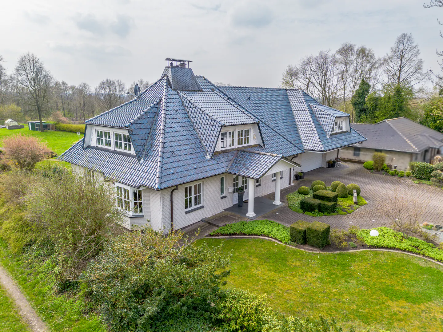 Aerial view of a white brick house with a blue tile roof, green lawn, and manicured hedges.
