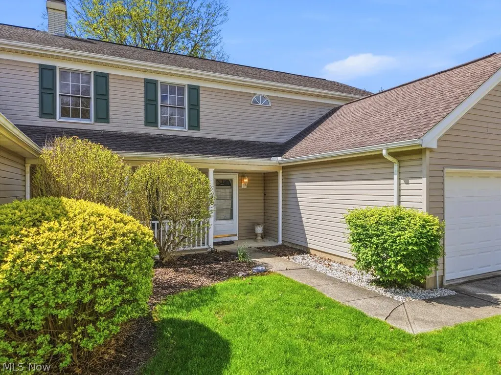 Beige two-story house with green shutters, a brown roof, and a green lawn.