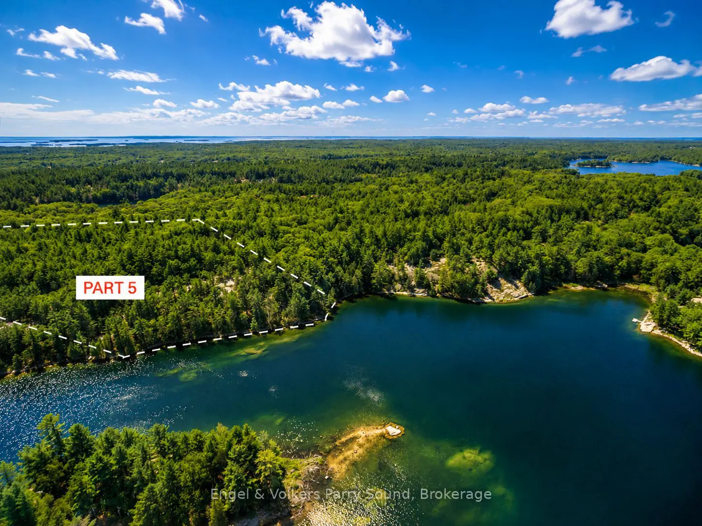 Aerial view of a wooded property, "Part 5", bordering a blue lake under a partly cloudy sky.