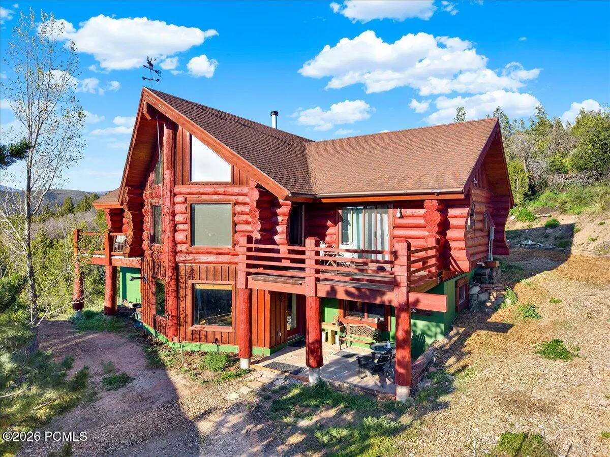 Two-story red log cabin with brown roof, balconies, and a weather vane against a blue sky with white clouds.