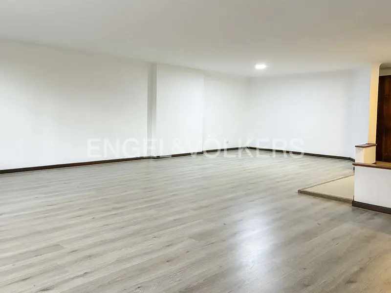 Bright, empty room with light gray wood floors, white walls, and dark brown trim. Engel & Völkers logo is visible.