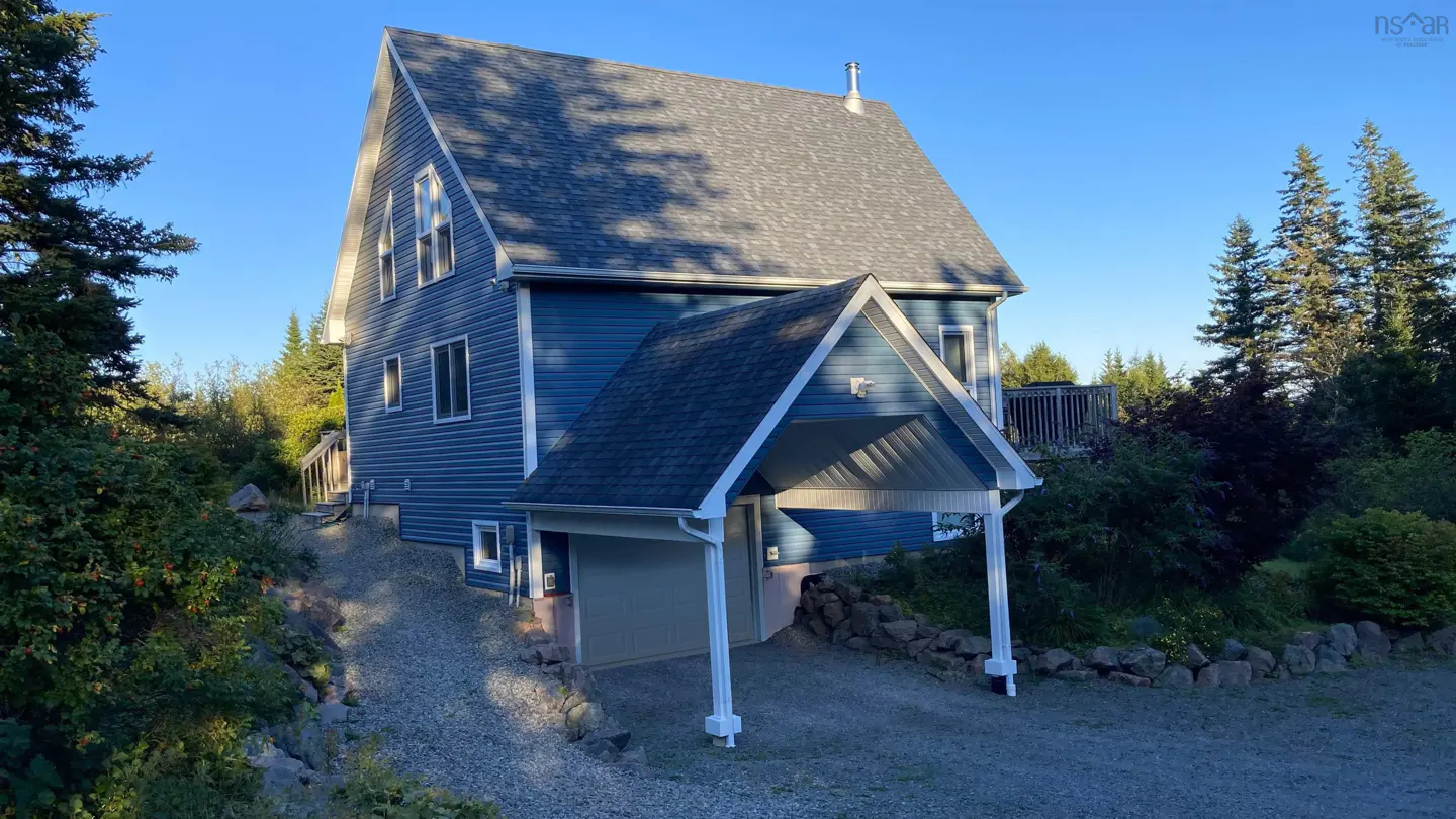 A two-story blue house with a gray roof and a carport is surrounded by trees.
