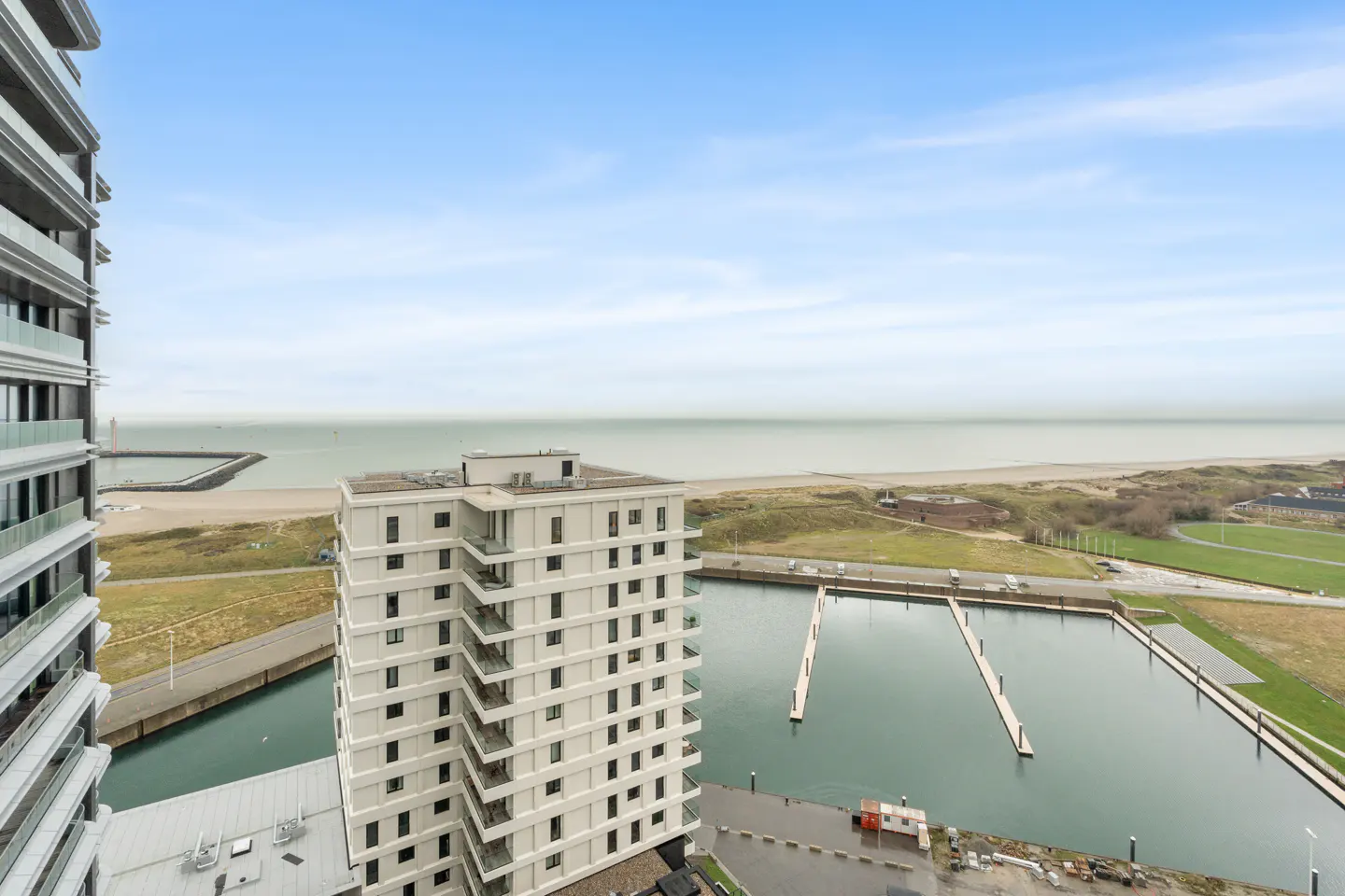 View of a marina and beach from a high-rise building. The sky is blue with some clouds.