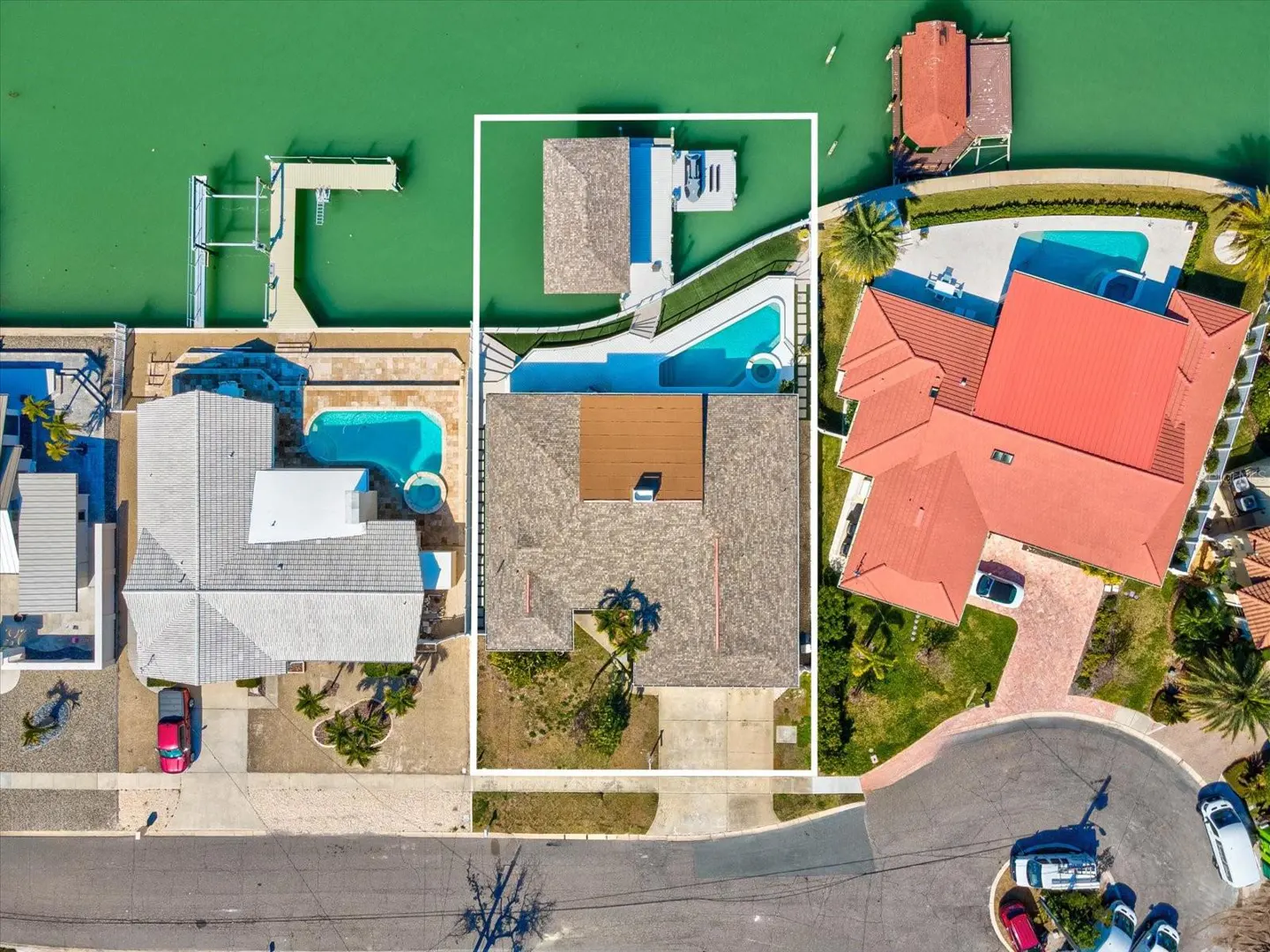 Aerial view of waterfront homes with pools, docks, and boat lifts on a sunny day.