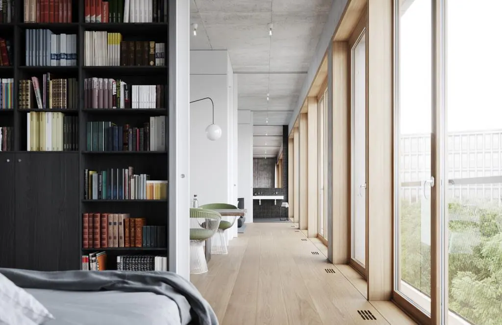 A modern apartment interior with a black bookcase, light wood floors, and large windows overlooking greenery.
