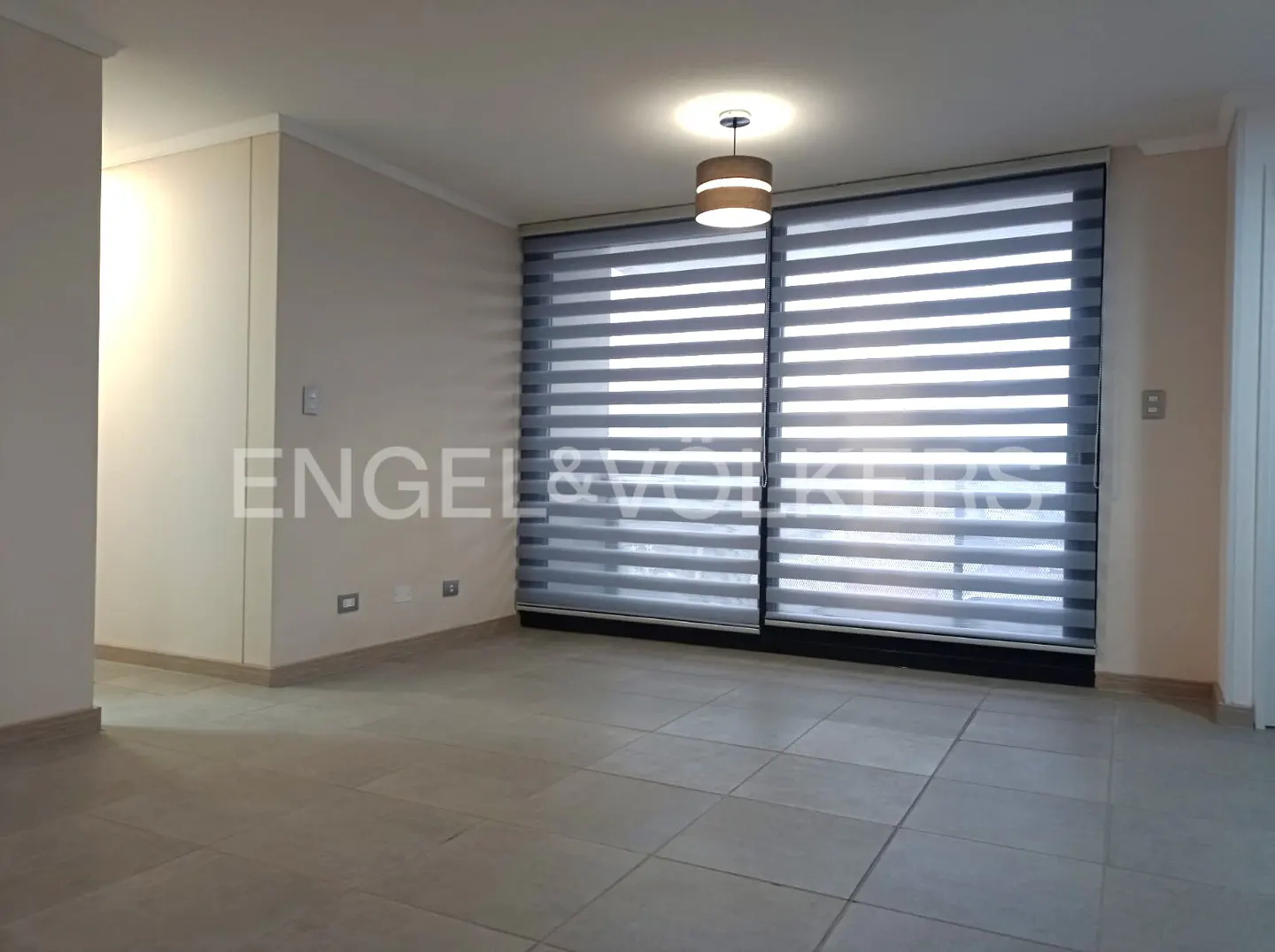 Empty room with light-colored tile floors, beige walls, and large windows covered by modern horizontal striped blinds.