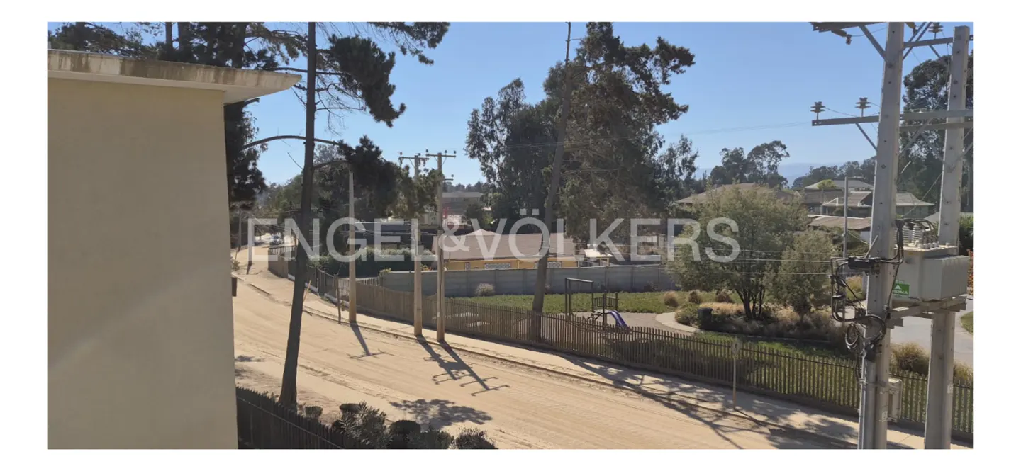 View from a building overlooking a dirt road, trees, and a playground on a sunny day. Power lines are visible.