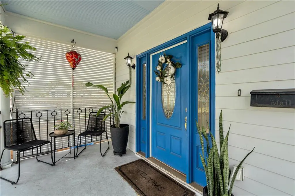 Front porch with a blue door, white siding, and black metal chairs. A welcome mat is in front of the door.