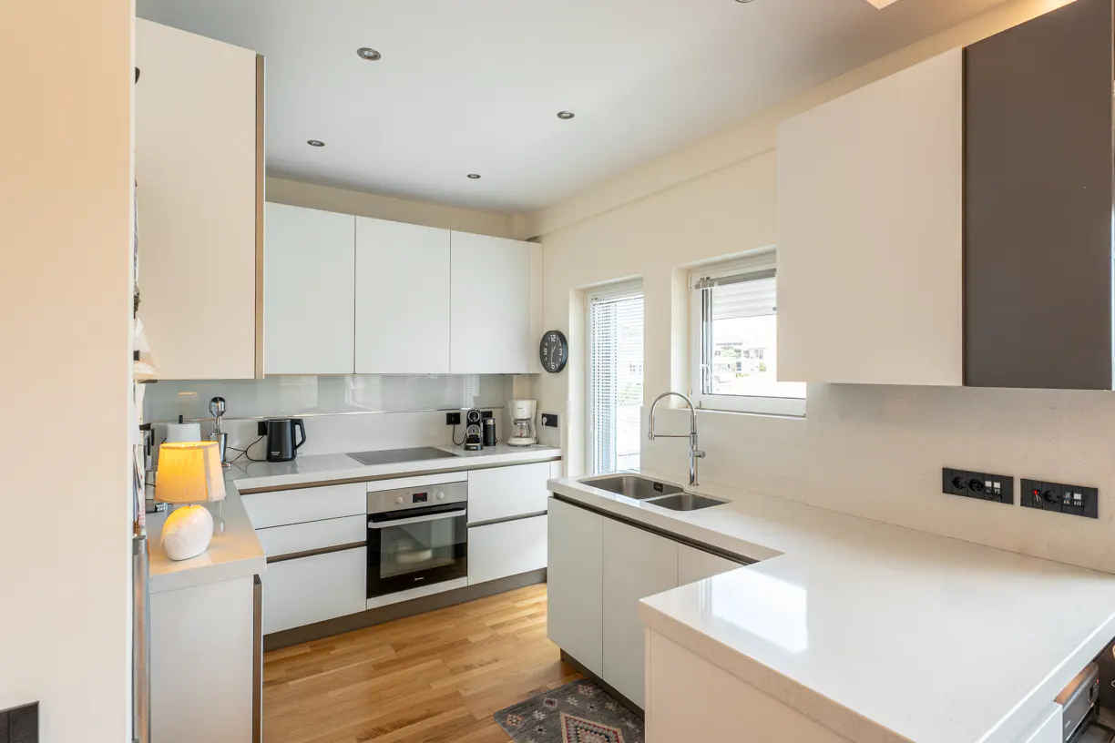 Modern kitchen with white cabinets, light wood floors, stainless steel appliances, and a white countertop.