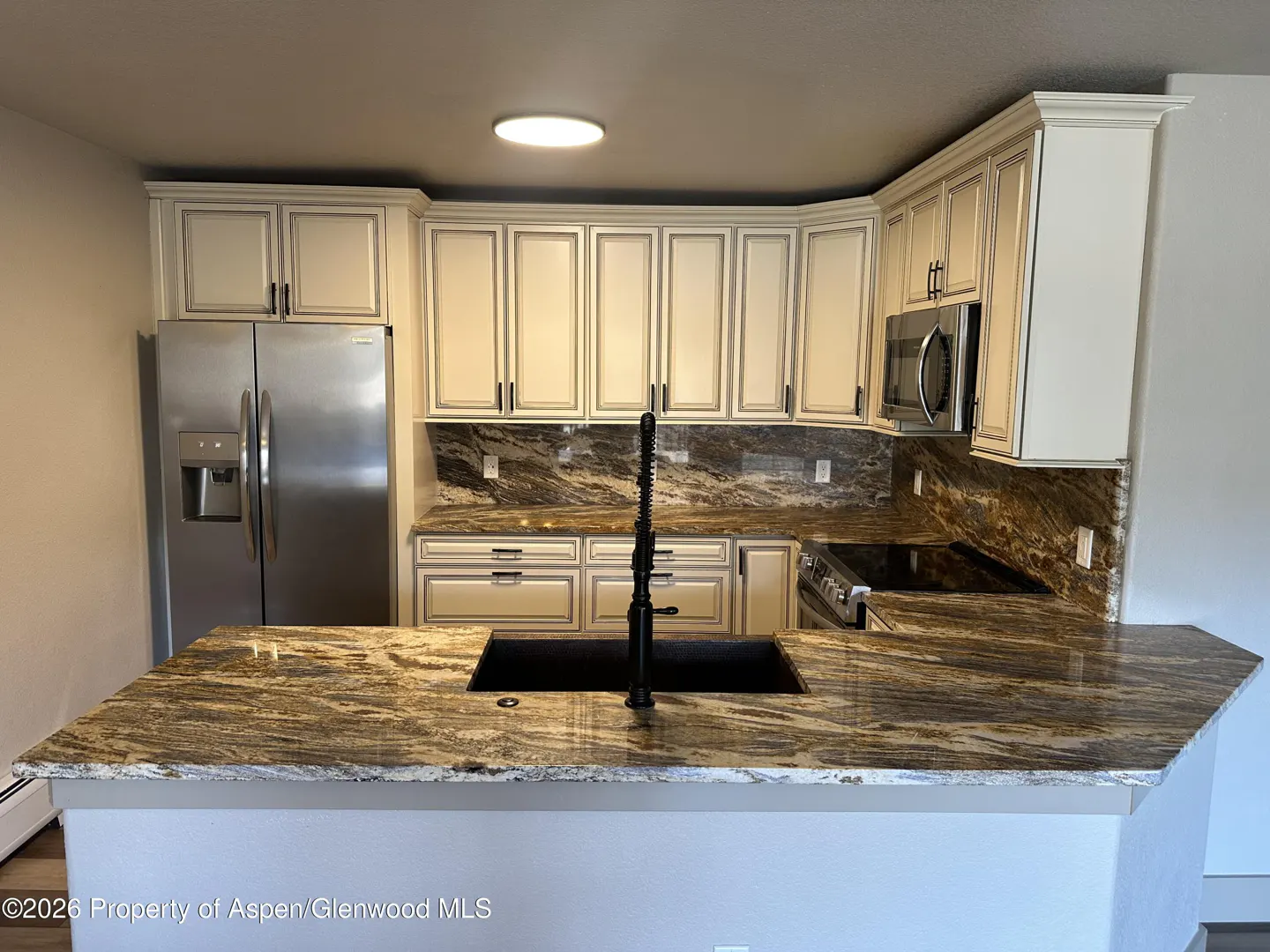 A kitchen with white cabinets, granite countertops, stainless steel appliances, and a black sink.