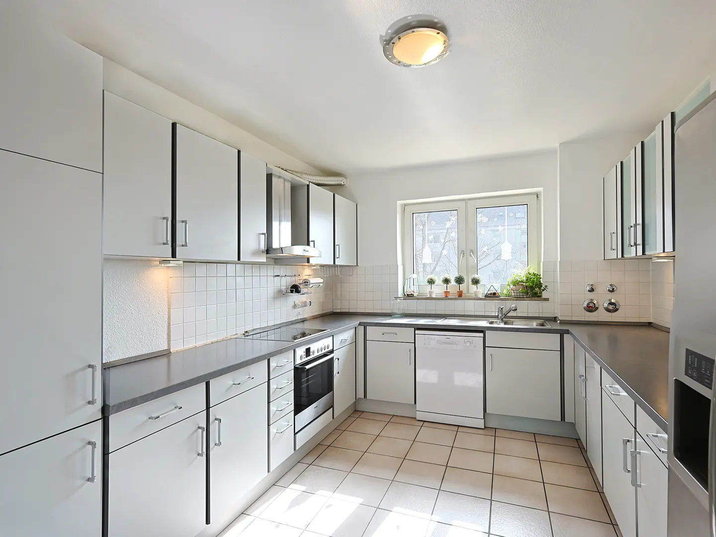 Bright kitchen with white cabinets, gray countertops, and tile flooring. A window above the sink offers natural light.