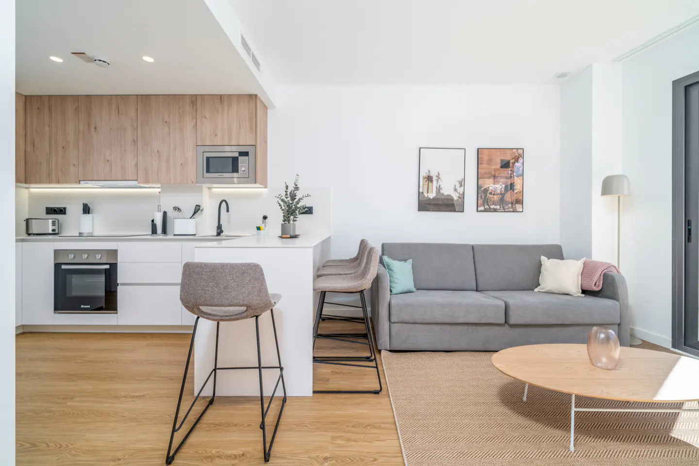 Bright, modern apartment with a kitchen island, gray sofa, and light wood floors. Two framed pictures hang above the sofa.
