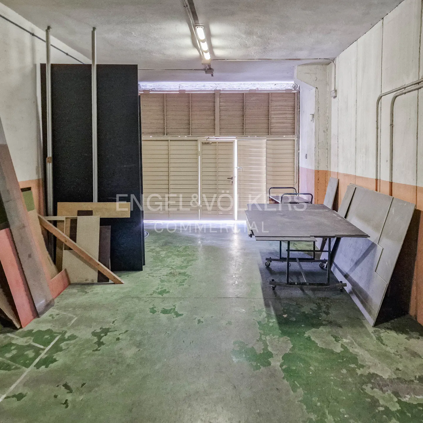 A commercial space with a table on wheels, wood panels, and a roll-up door.