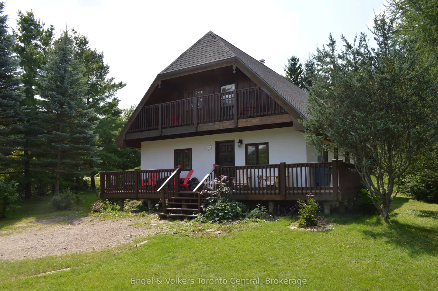 Two-story white house with a brown roof and wooden decks, surrounded by green trees and grass.