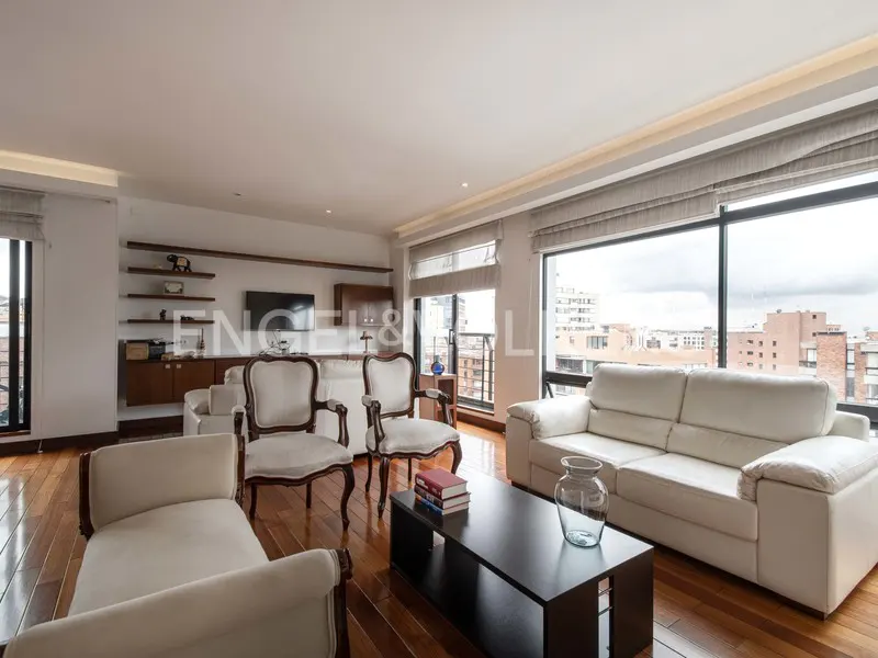 Bright living room with hardwood floors, white sofas and chairs, a black coffee table, and large windows with city views.