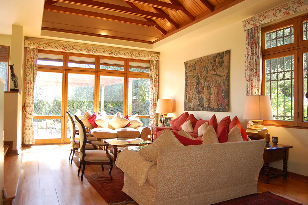 Living room with wood floors, sofas with red pillows, and a tapestry on the wall. Large windows let in natural light.