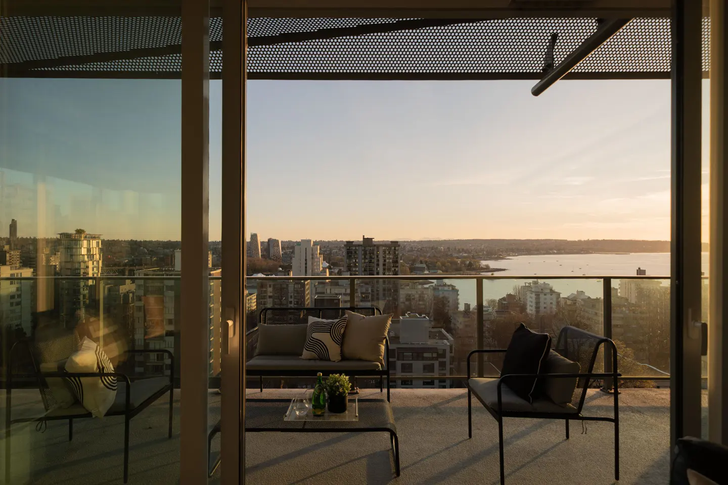 Balcony view of a city skyline at sunset. Modern furniture, including a loveseat and chairs, are arranged on the balcony.