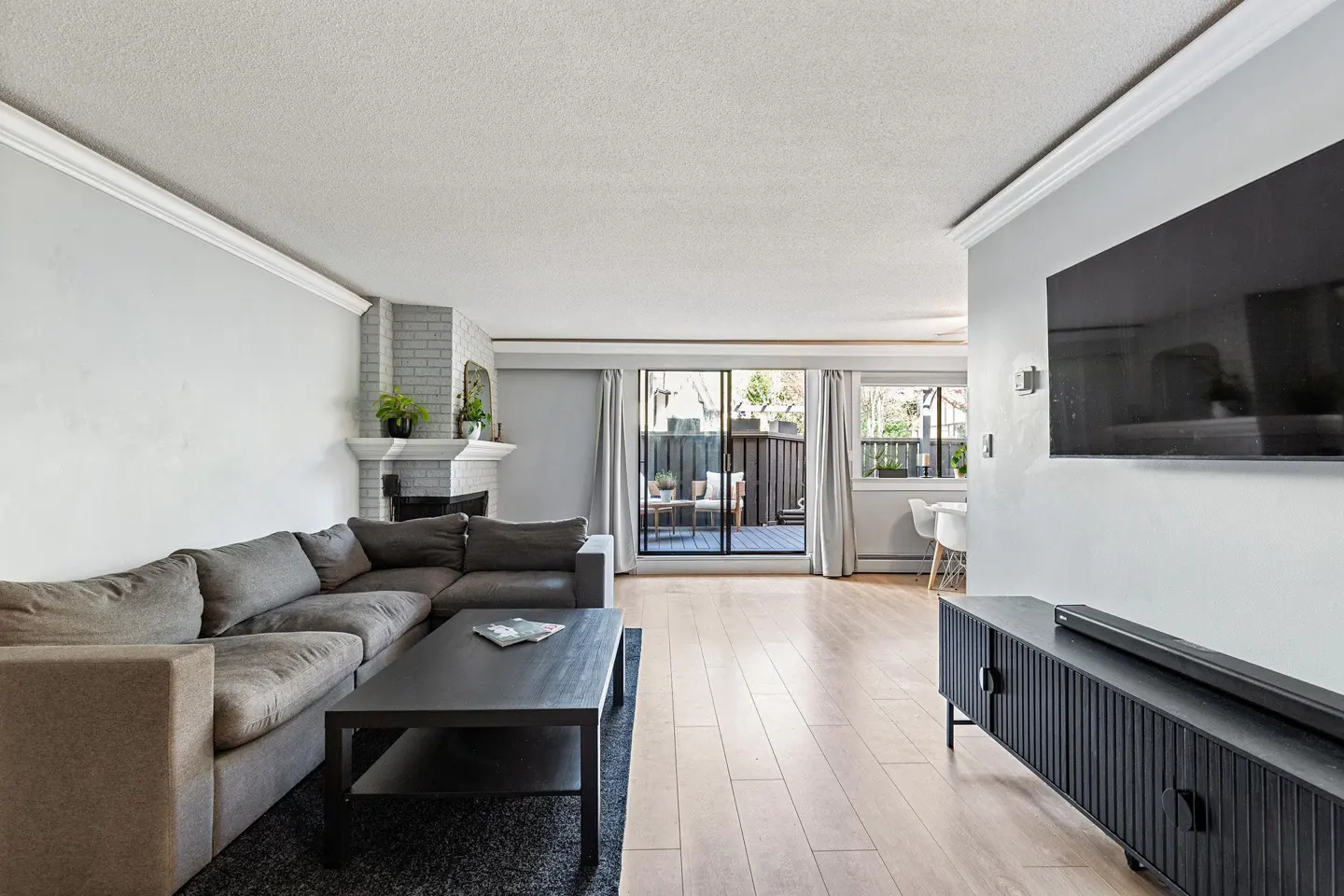 Modern living room with grey sectional sofa, black coffee table, TV, and sliding glass doors leading to a patio.