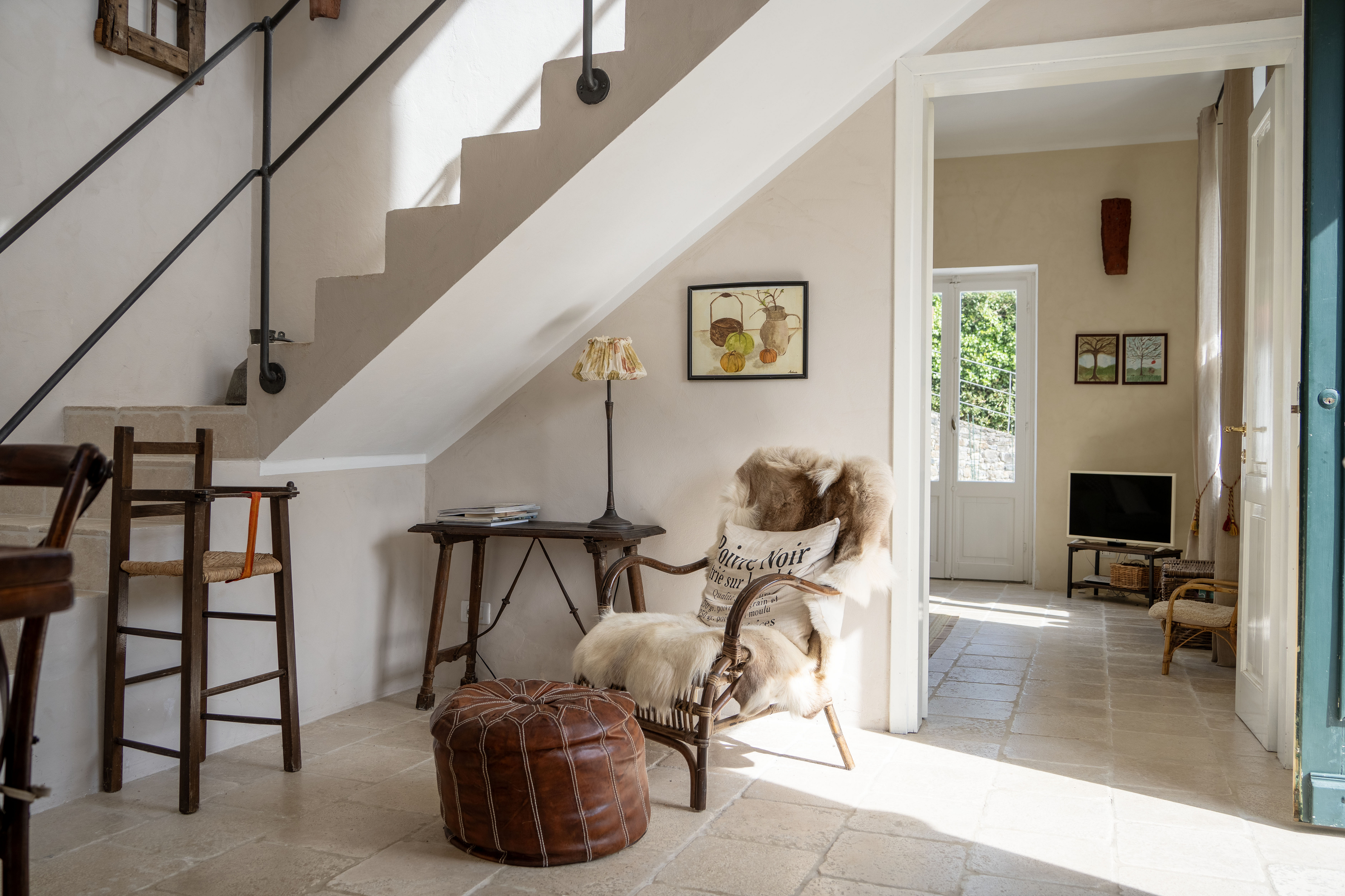 Interior view of a home with stone floors, stairs, and a doorway leading to a living room with a TV. A chair and ottoman sit near the stairs.