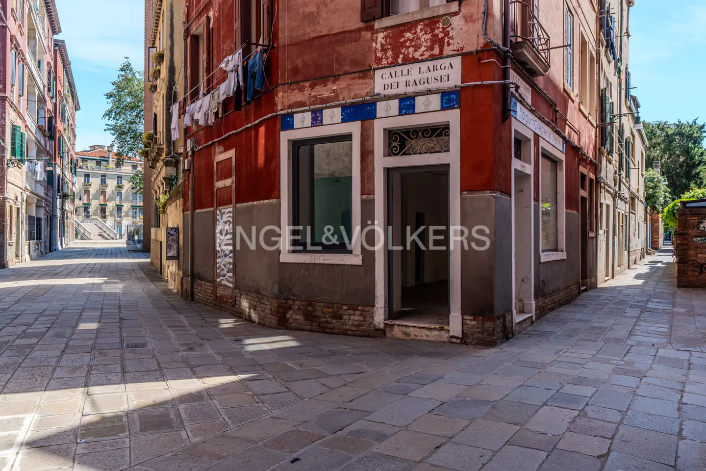 A street view in Venice, Italy, with red and gray buildings, stone streets, and an open doorway.