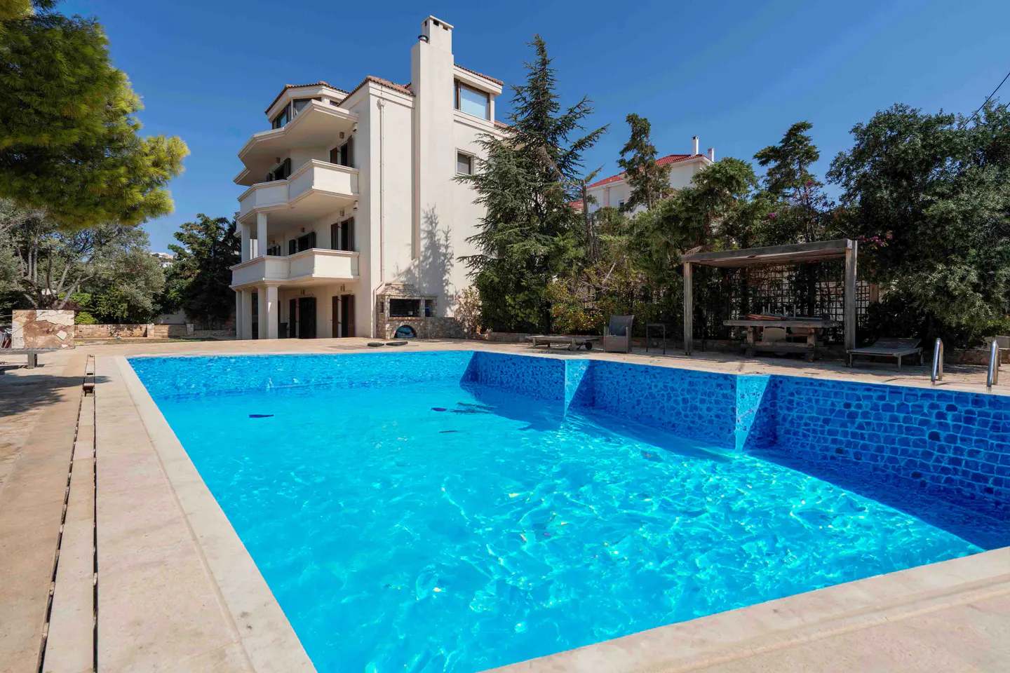 Exterior view of a white three-story house with a blue tiled swimming pool in the foreground.