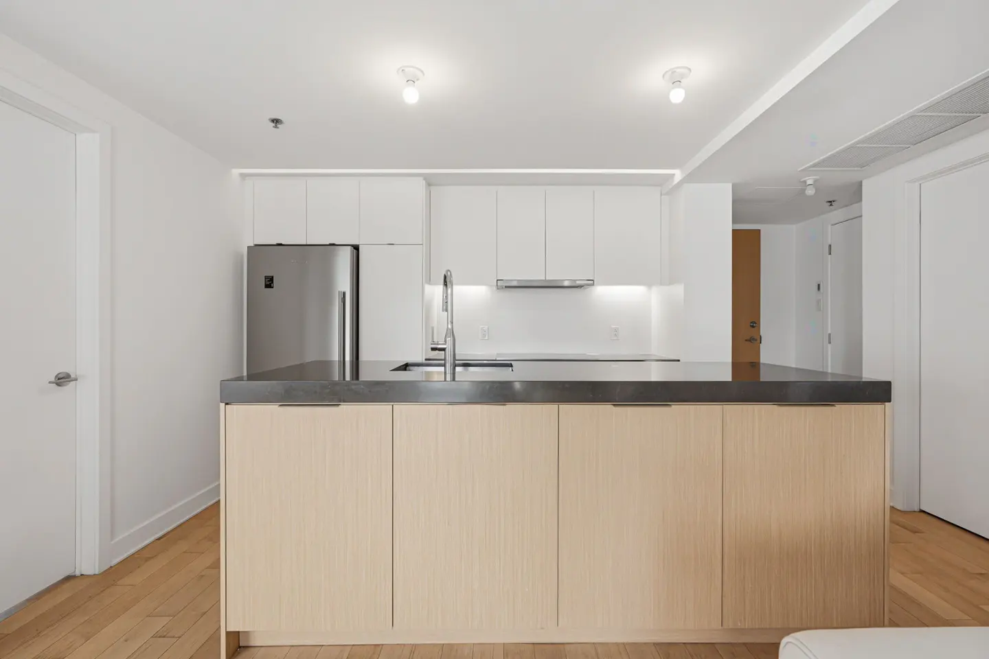 Modern kitchen with light wood island, dark countertop, white cabinets, stainless steel fridge, and hardwood floors.