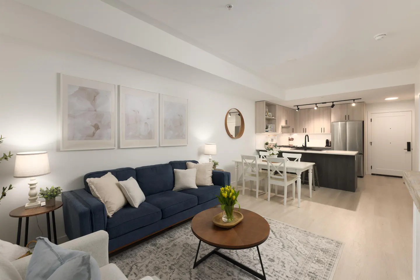 Bright, open-concept living space with a blue sofa, wood coffee table, and kitchen with stainless steel appliances.