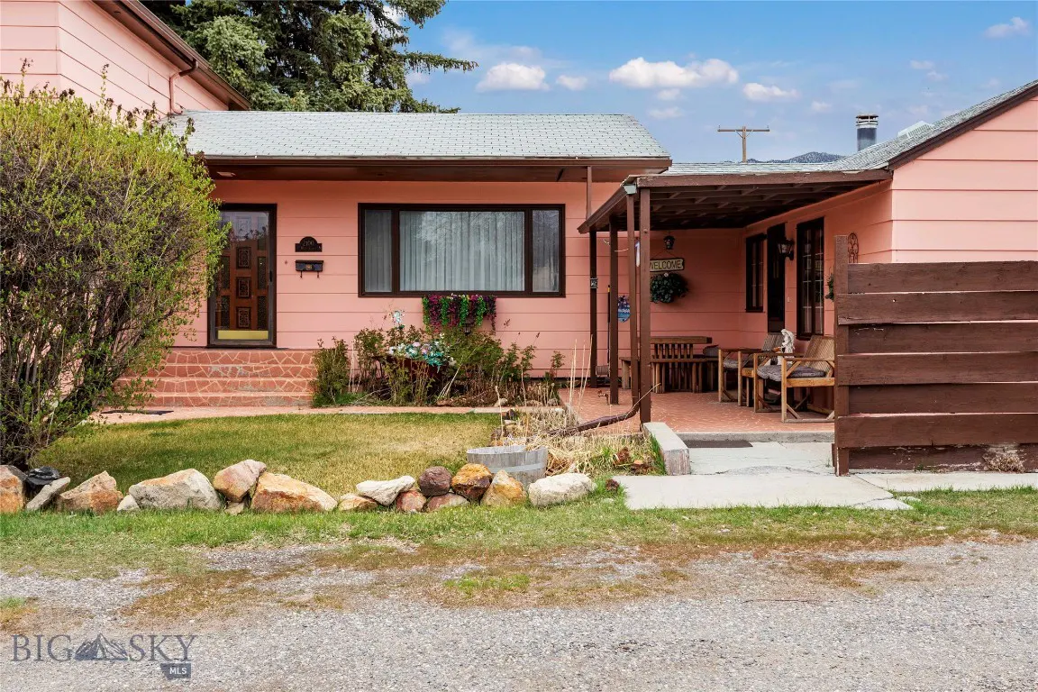 Single-story peach-colored house with a covered patio, brown privacy fence, and a front yard with a rock border.