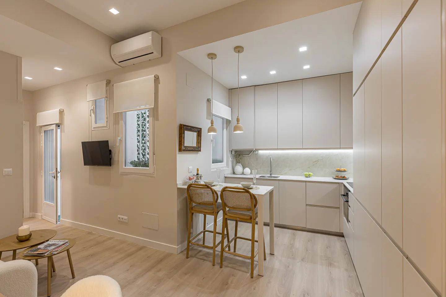 Bright, modern apartment interior with a small kitchen, bar stools, and living area in neutral tones.