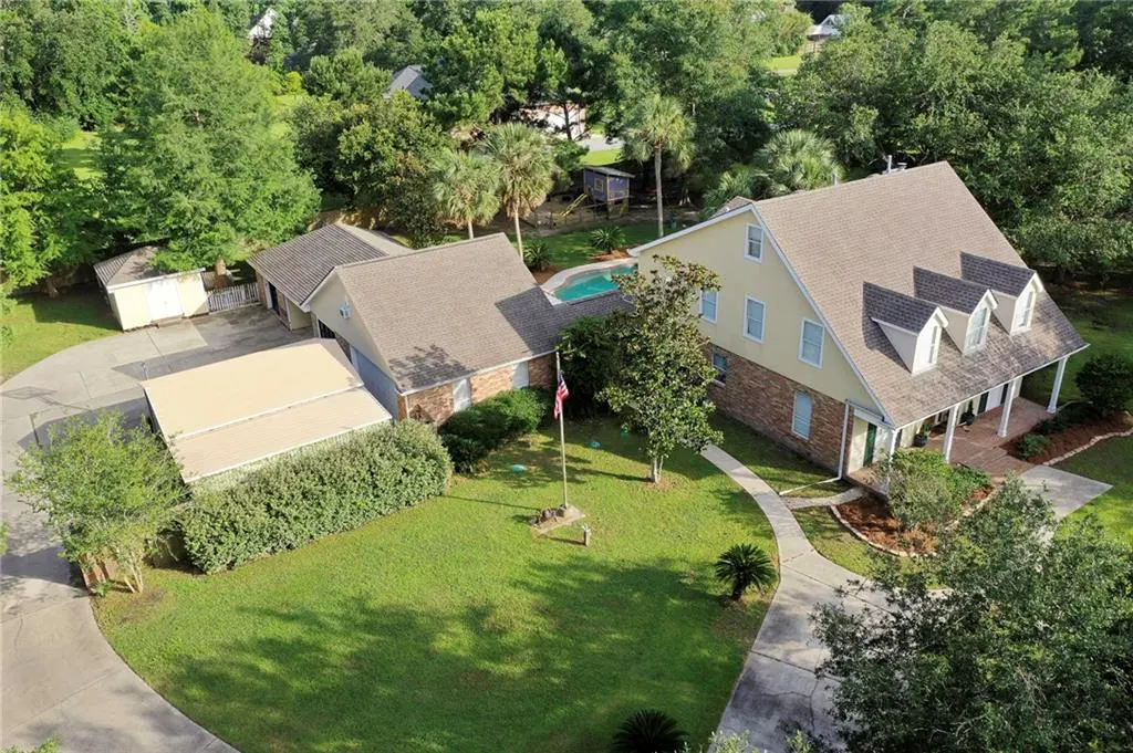 Aerial view of a yellow two-story home with a pool, detached garage, and large green yard in a wooded neighborhood.