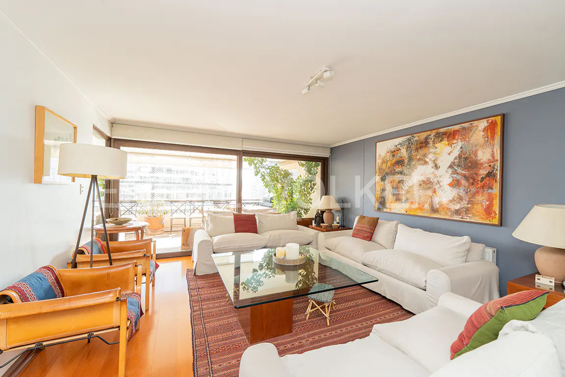 Bright living room with white sofas, leather armchairs, a glass coffee table, and large abstract art on a blue wall.