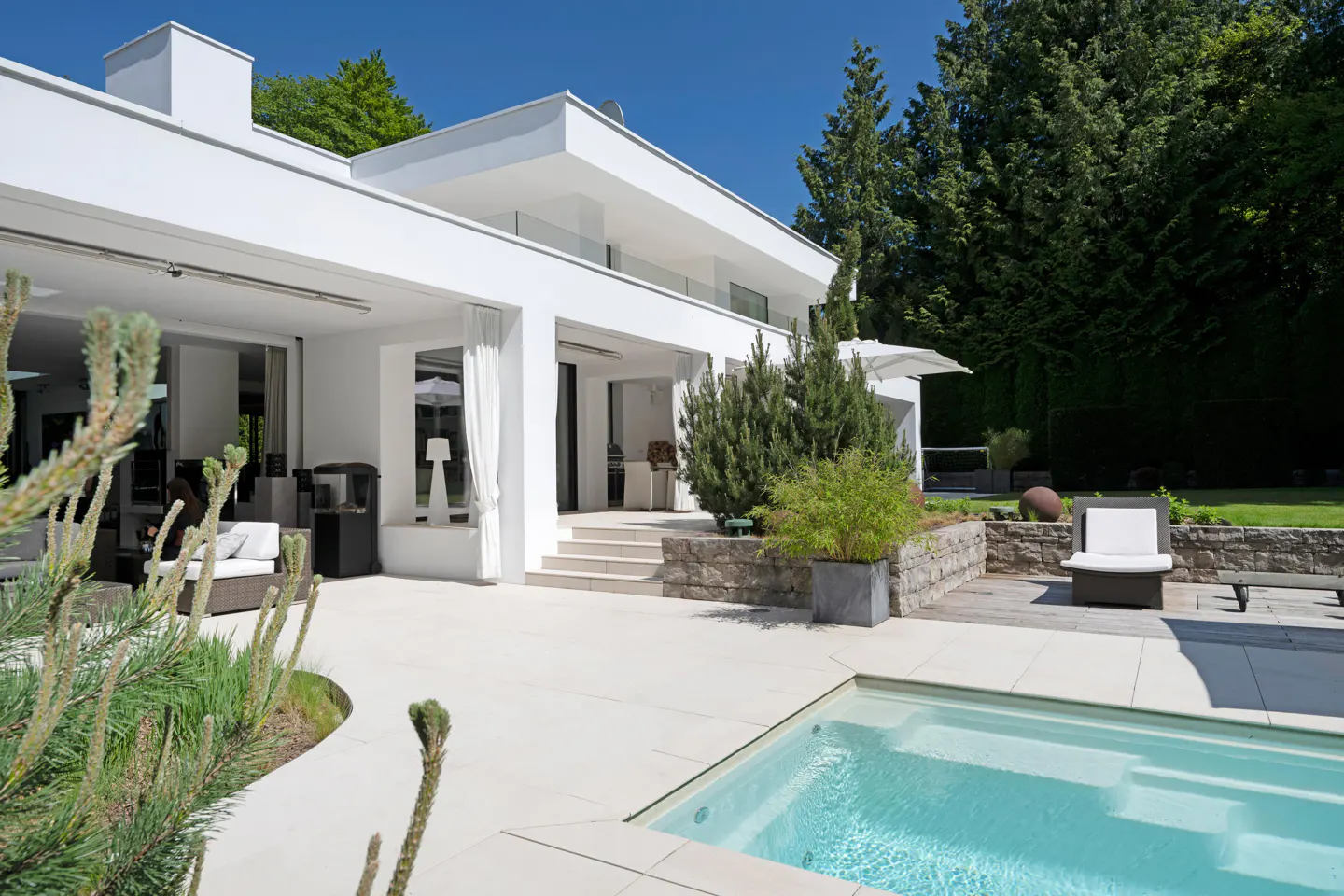 Modern white house with a pool and patio. Trees are in the background.