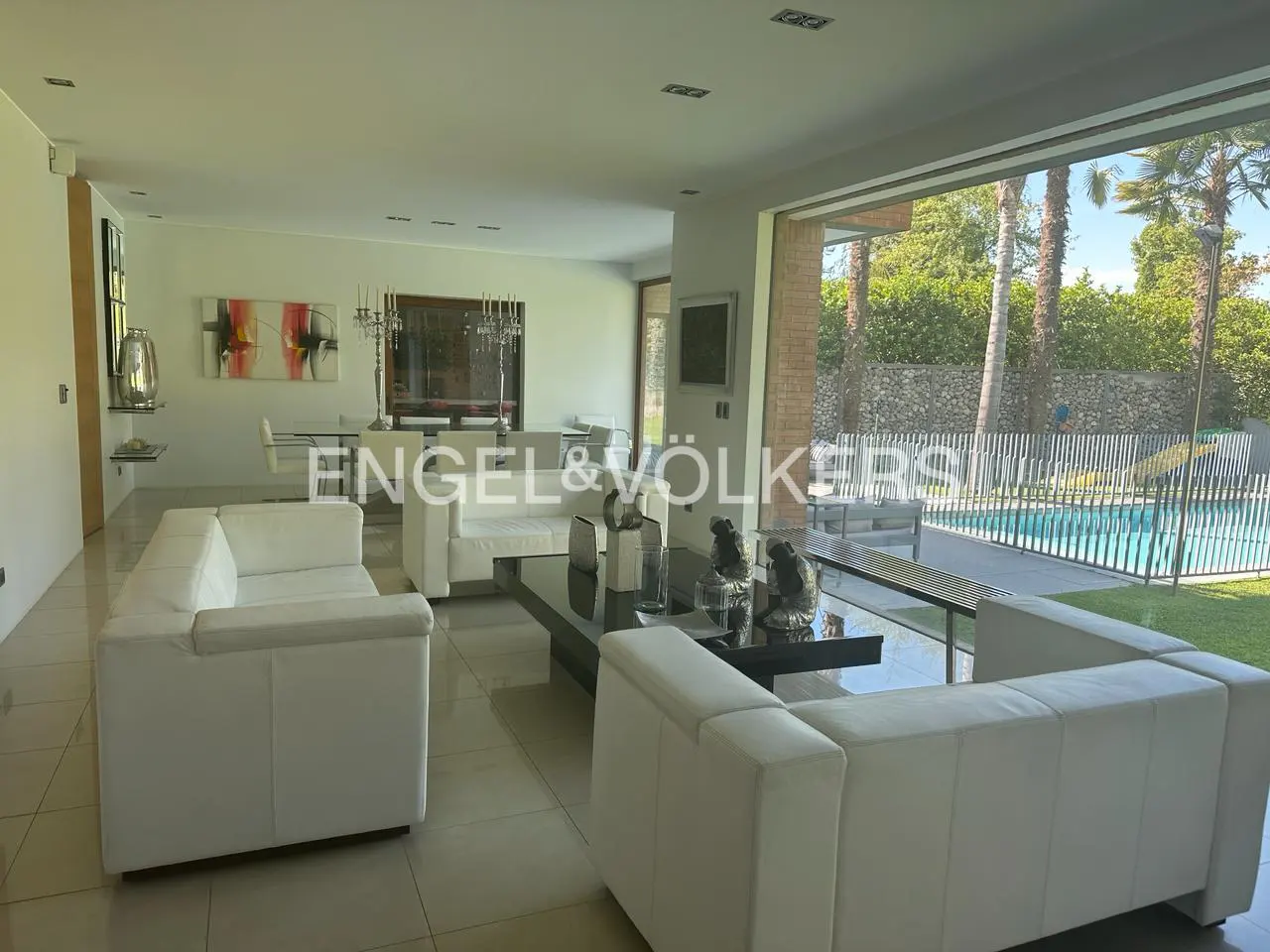 Bright living room with white sofas, a black coffee table, and a view of a pool through a large window.