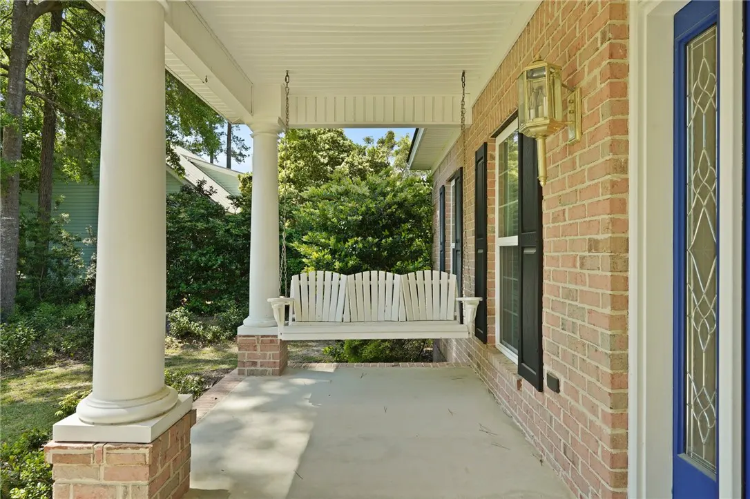 Covered porch with a white swing hanging from the ceiling, brick pillars, and a blue front door.