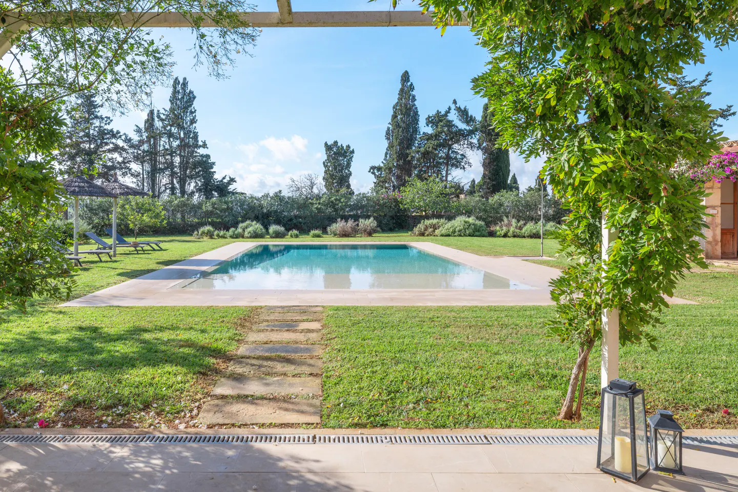 A rectangular pool is centered in a green lawn, with trees and lounge chairs in the background.