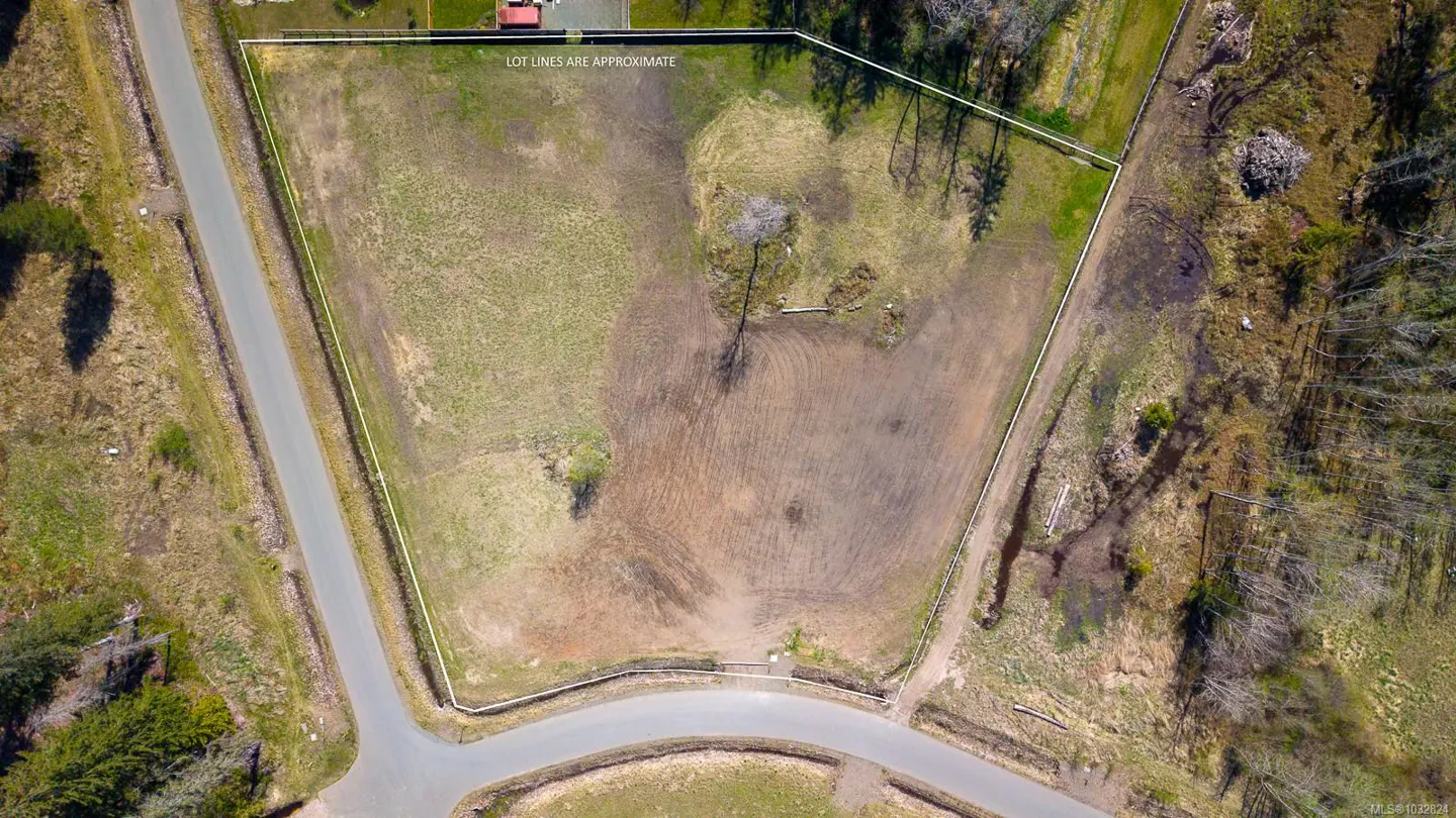 Aerial view of a vacant lot with approximate lot lines marked in white, bordered by roads and trees.