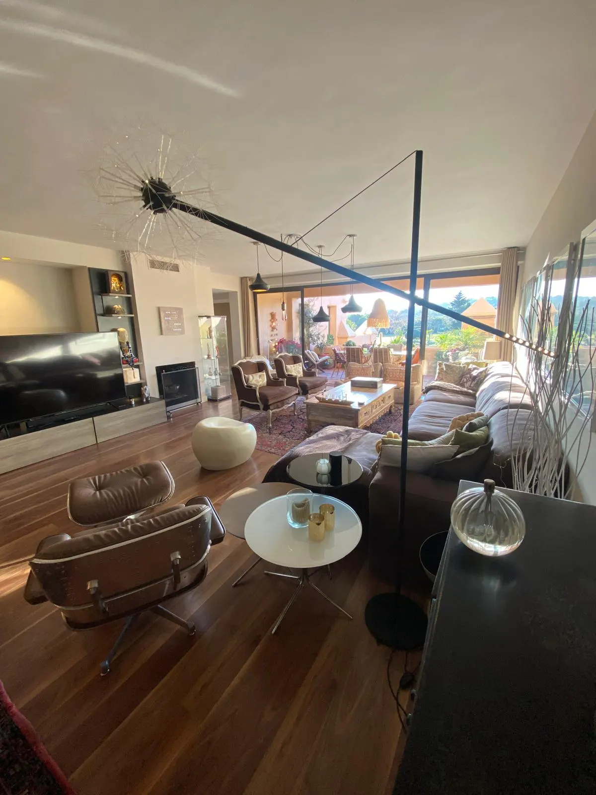 A spacious living room with hardwood floors, brown leather furniture, and a large window overlooking a scenic view.