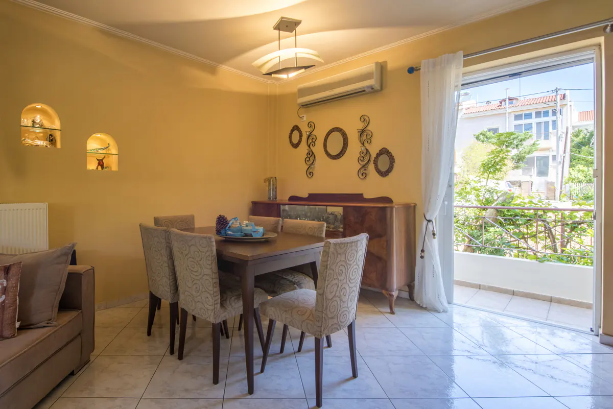 Dining room with yellow walls, wooden table, four patterned chairs, wall decor, and a glass door leading to a balcony.