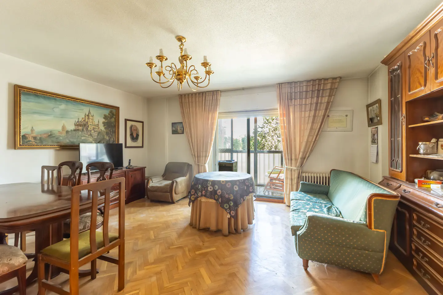 A living room with a dining table, sofa, armchair, and a balcony with natural light.